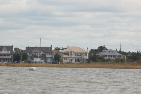 1990 Ford Bronco - Several large houses line the shore, viewed across the water under an overcast sky.
