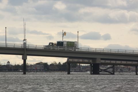 1990 Ford Bronco - A truck transports portable toilets across a bridge over choppy water under a cloudy sky.