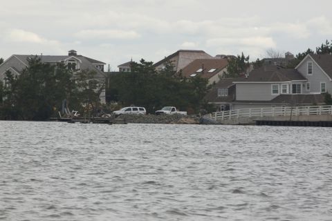 1990 Ford Bronco - Two vehicles are visible on land near waterfront houses under an overcast sky.