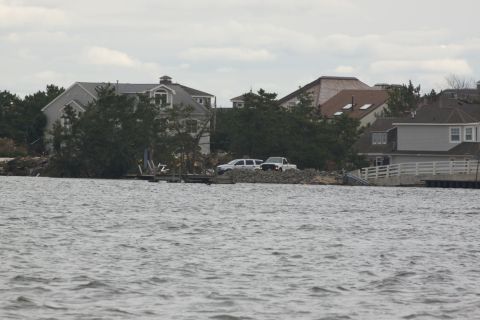 1990 Ford Bronco - Two vehicles are visible parked on land near houses and trees, with a body of water in the foreground.