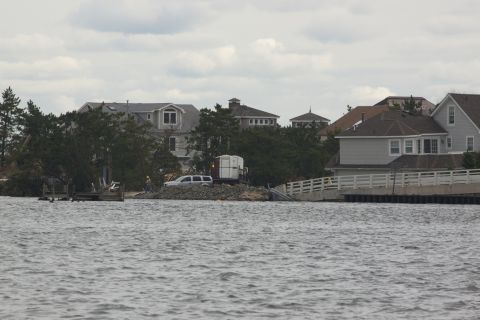 1990 Ford Bronco - SUV parked near water with houses and trees in background under cloudy sky.
