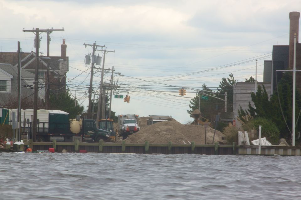 Construction scene with trucks, portable toilets, and sand piles by the water