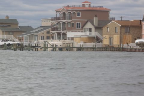 1990 Ford Bronco - A waterfront scene shows houses with boarded windows and docked boats, some of which appear to be damaged or submerged.