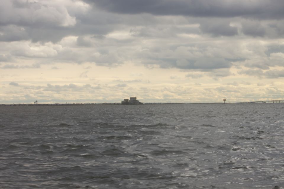 Water under a cloudy sky with distant buildings and a bridge