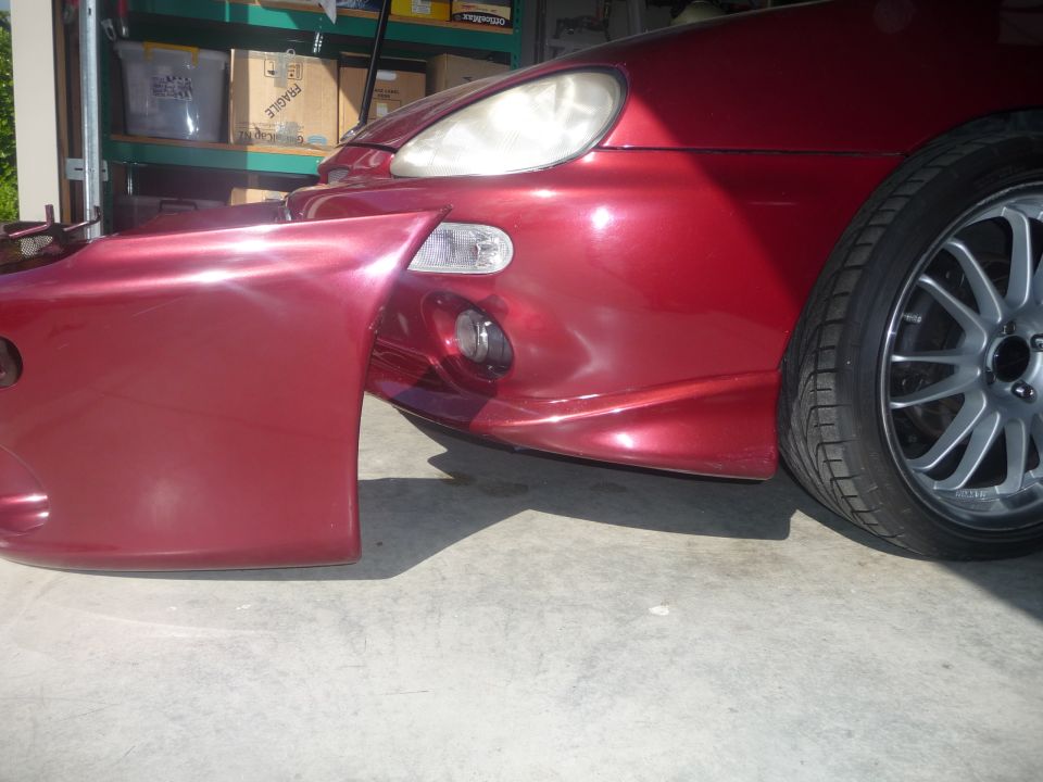 Front corner of dark red sport coupe with fog light and gray alloy wheel in garage