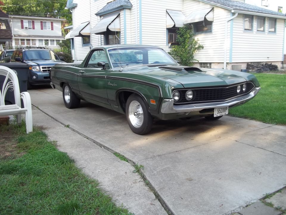 Green 1970 Ford Ranchero parked on driveway, blue SUV behind it