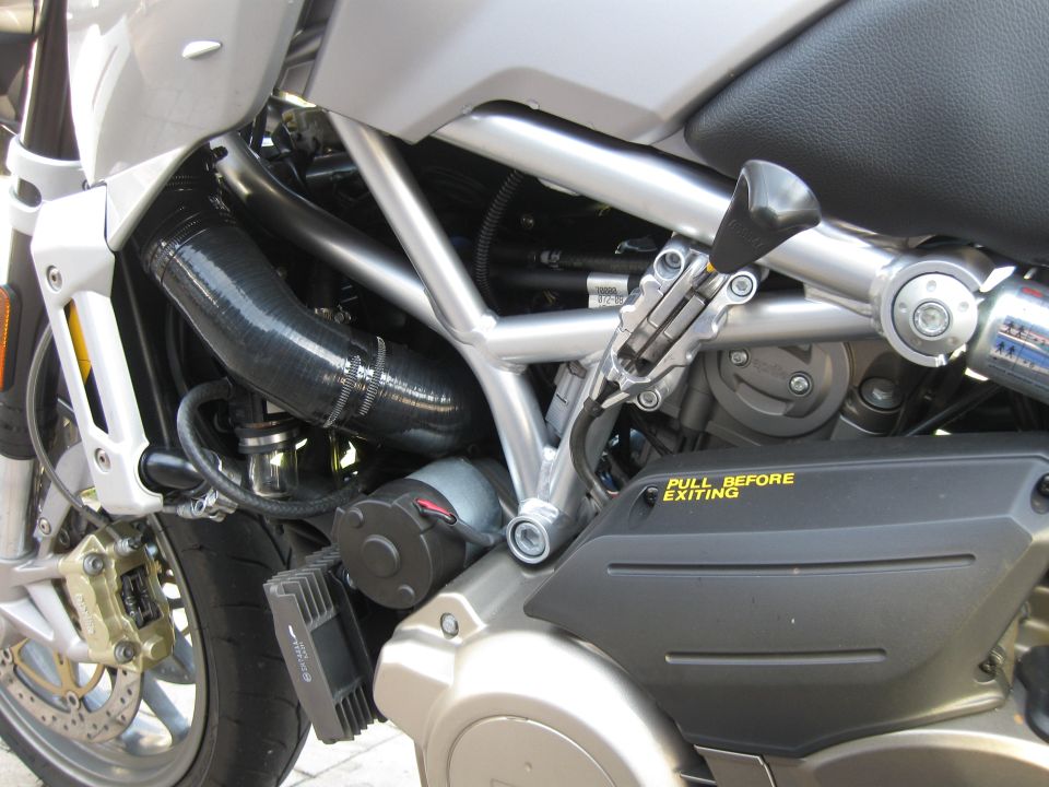 Close-up of motorcycle engine, frame, and exhaust pipe. Yellow text reads 'PULL BEFORE EXITING'