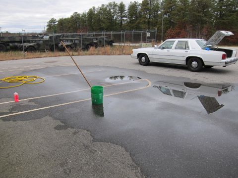1991 Ford LTD Crown Victoria - A white sedan sits in a parking lot with puddles reflecting the sky and the car.