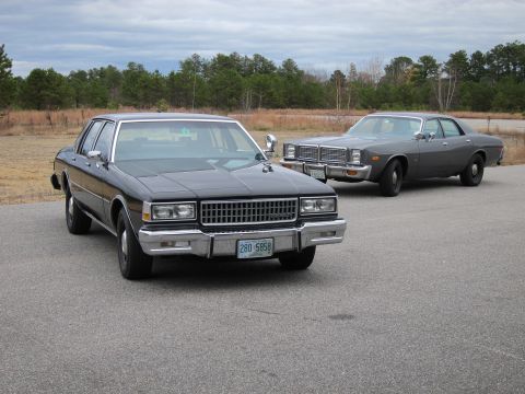 1991 Ford LTD Crown Victoria - Two full-size sedans from the late 1970s are parked side-by-side on an asphalt lot.