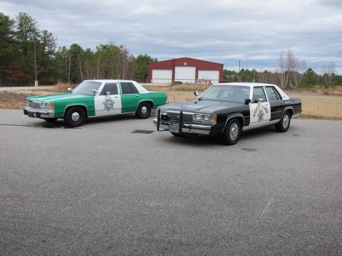 1991 Ford LTD Crown Victoria - Two older model police sedans are parked side-by-side outdoors.