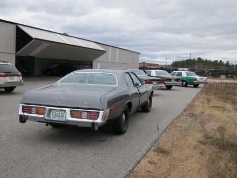 1991 Ford LTD Crown Victoria - Rear view of a 1974 Dodge Monaco sedan with other vehicles and a large building in the background.