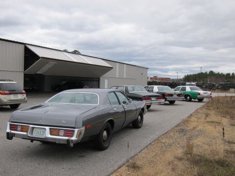 1991 Ford LTD Crown Victoria - Several cars are parked in a line outside a large building with an open garage door.