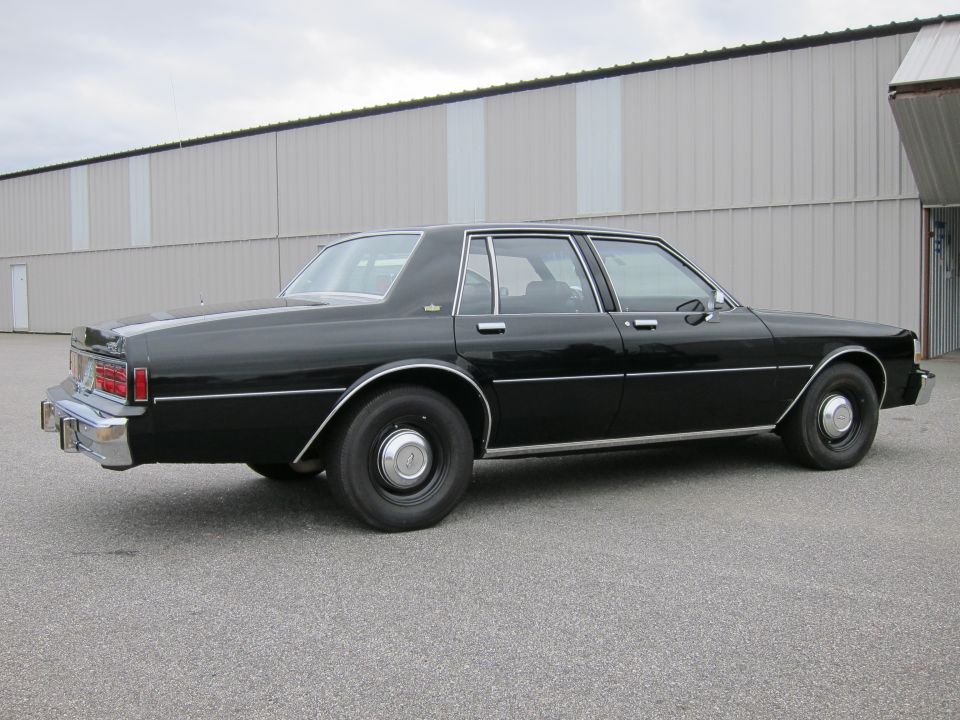 Black sedan with chrome trim parked on asphalt in front of a corrugated metal building