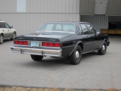 1991 Ford LTD Crown Victoria - Rear view of a black Chevrolet Caprice sedan parked on asphalt in front of a metal building.