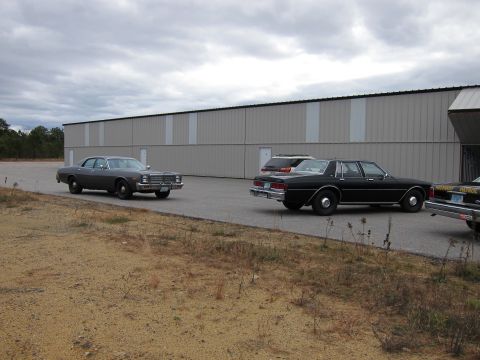 1991 Ford LTD Crown Victoria - Several vehicles are parked in a lot next to a large industrial building.