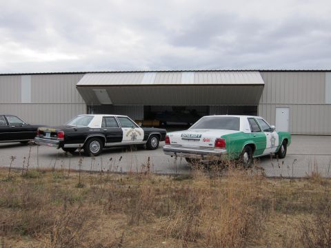 1991 Ford LTD Crown Victoria - Two sheriff's department vehicles are parked in front of a large hangar on an overcast day.