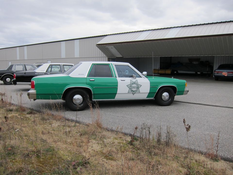 Green and white Ford Crown Victoria with a sheriff's star emblem on the side, parked outdoors