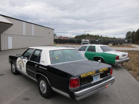 1991 Ford LTD Crown Victoria - Two police cars, a black and white and a green and white, are parked outside a building.