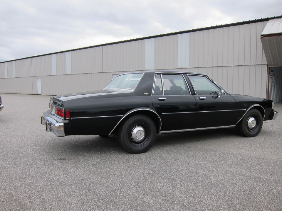 Black sedan parked on asphalt in front of a large industrial building