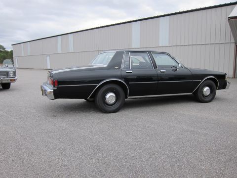 1991 Ford LTD Crown Victoria - A black sedan is parked on asphalt in front of a long, light-colored building.