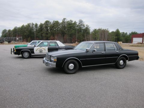 1991 Ford LTD Crown Victoria - Two police sedans, one black and one marked Highway Patrol, parked on asphalt.