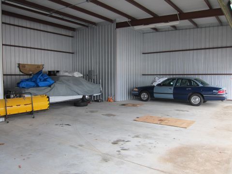 1991 Ford LTD Crown Victoria - Two sedans are parked inside a metal garage, one covered and the other partially repainted.
