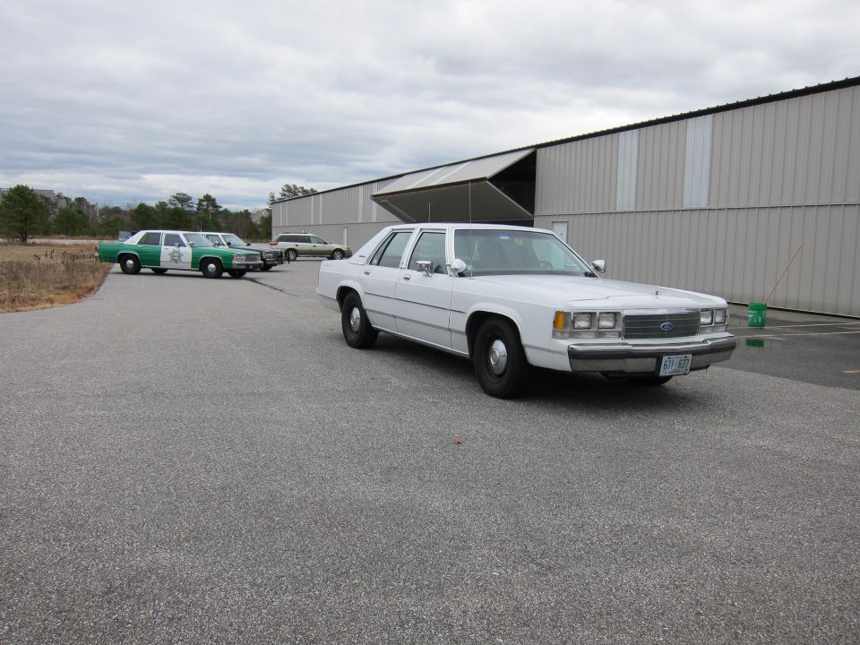 White sedan parked on asphalt, front 3/4 view. License plate visible