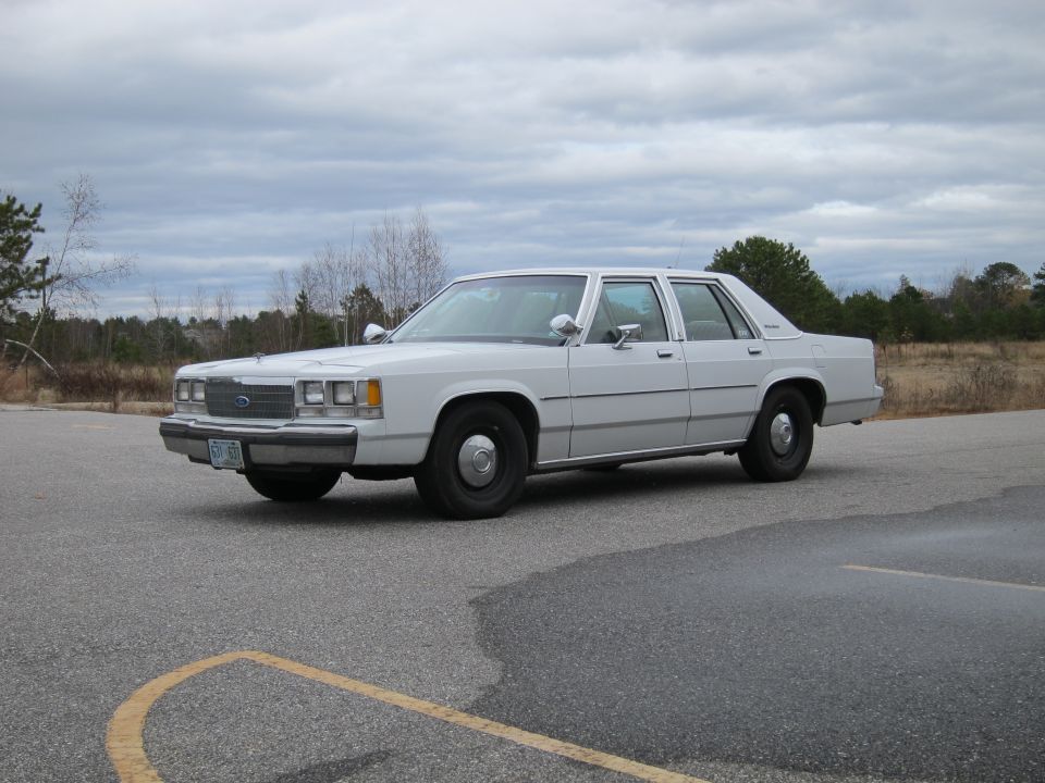White sedan parked on asphalt, front 3/4 view. The car has a boxy body style and chrome trim