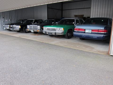 1991 Ford LTD Crown Victoria - Several sedans, including a 1991 Ford Crown Victoria LTD, are parked in a covered bay.
