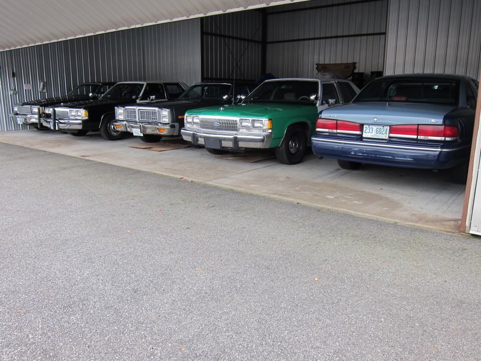 1991 Ford Crown Victoria LTD and other sedans parked in a row under a metal carport