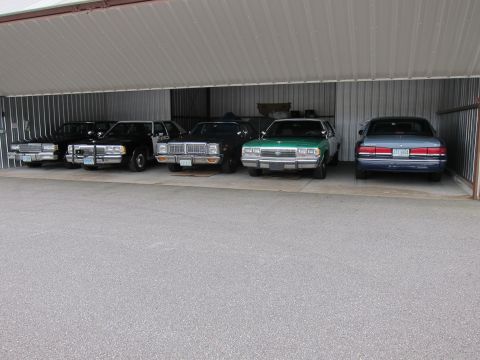 1991 Ford LTD Crown Victoria - A collection of sedans are parked side-by-side in a storage area.