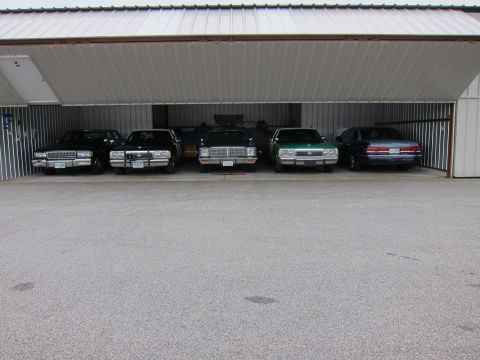 1991 Ford LTD Crown Victoria - Several sedans are parked inside a large garage with the door open.