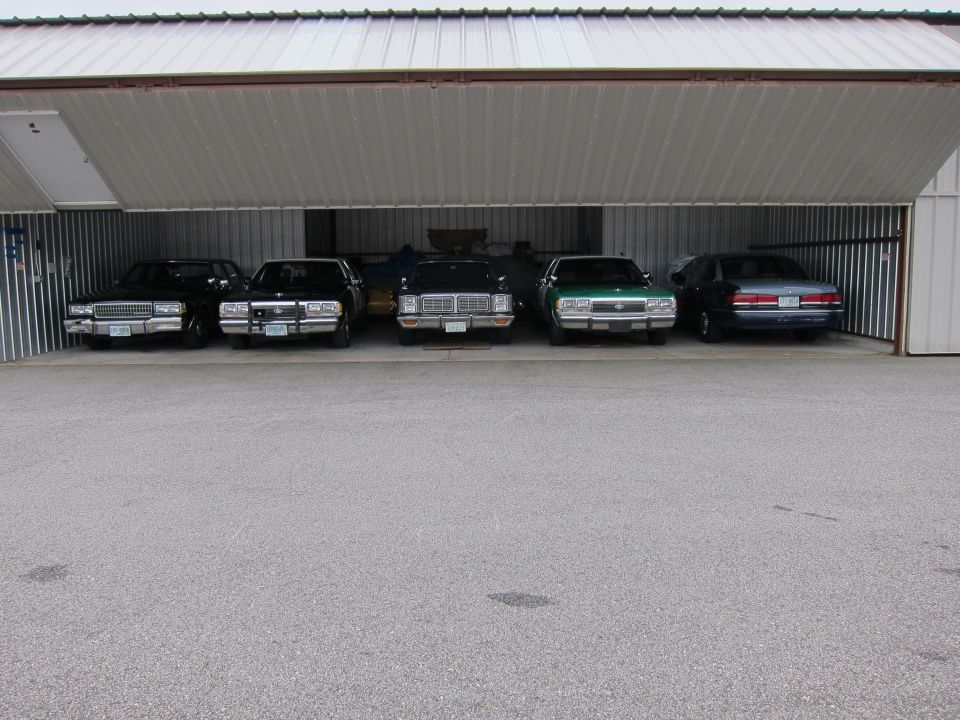 Five sedans parked in a row inside a metal garage, viewed from the front