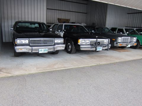 1991 Ford LTD Crown Victoria - Multiple sedans are parked in a row inside a metal-sided garage.
