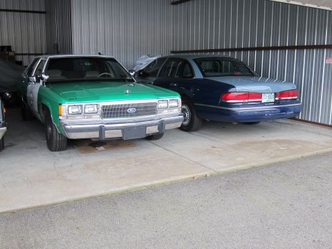 1991 Ford LTD Crown Victoria - Two Ford Crown Victorias are parked side-by-side inside a metal-sided garage.