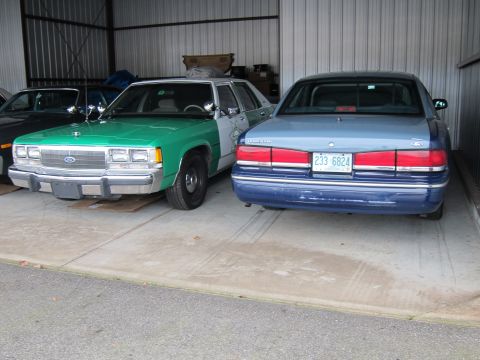 1991 Ford LTD Crown Victoria - Two sedans are parked side-by-side inside a garage, with one showing its front end and the other its rear.