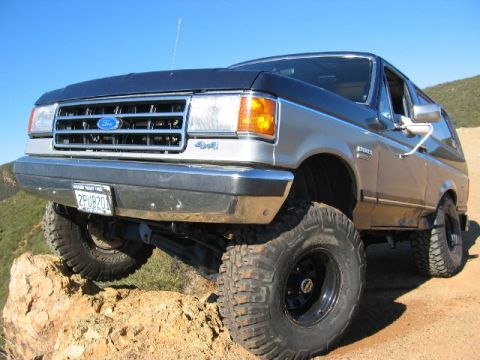 1989 Ford Bronco - This lifted Ford Bronco is positioned on a steep, rocky trail under a clear blue sky.