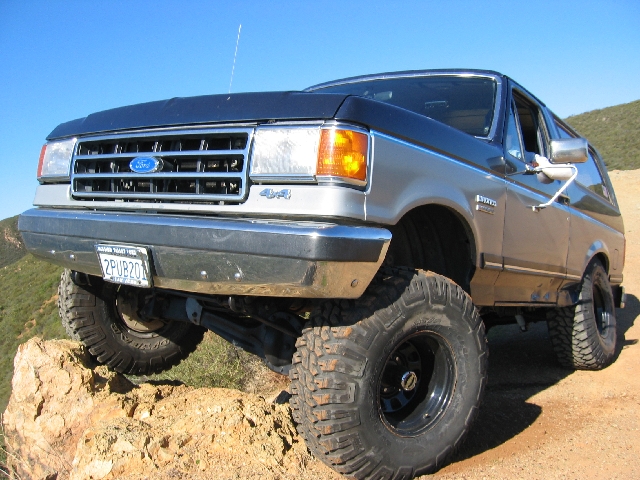 Lifted gray Ford Bronco with mud tires and black wheels on a dirt trail