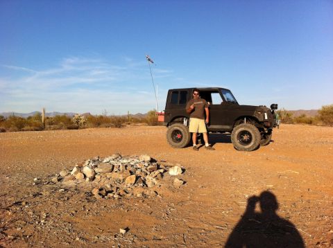 1987 Suzuki Samurai - A man poses next to a dark 1987 Suzuki Samurai in a dry, arid landscape under a clear blue sky.