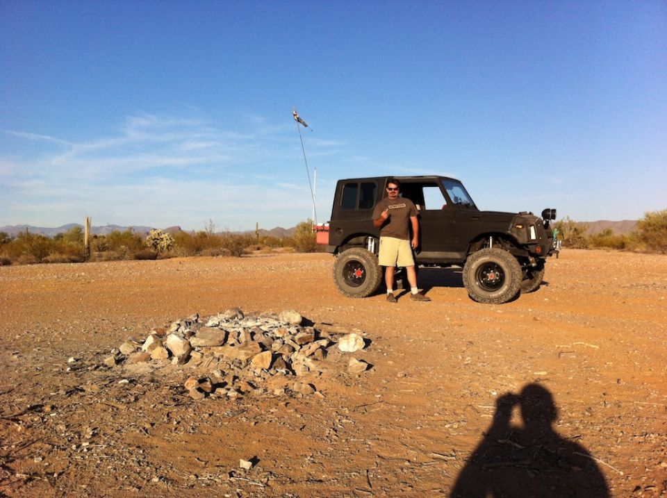 Dark 1987 Suzuki Samurai parked in desert with man standing beside it