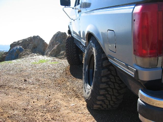 Silver Ford Bronco rear quarter with lifted suspension and mud tires on dirt near rocks