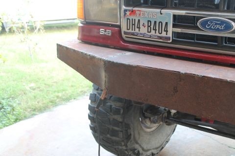 1990 Ford Bronco - A custom, heavy-duty bumper is fitted to the front of a red Ford truck, obscuring the original grille.