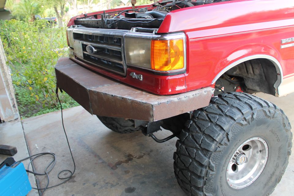 Red truck front with custom bumper and large tires. 4x4 badge visible