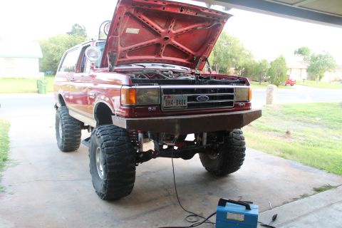 1990 Ford Bronco - This red 1990 Ford Bronco features a custom bumper and lifted suspension, with its hood open.