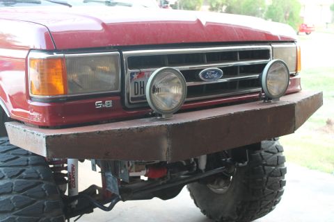 1990 Ford Bronco - Custom bumper on a red Ford truck, auxiliary lights and a prominent Ford emblem on the grille.
