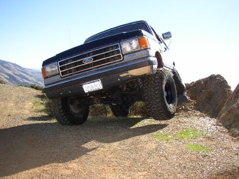 1989 Ford Bronco - This lifted Ford truck navigates a rocky, off-road path under a clear blue sky.