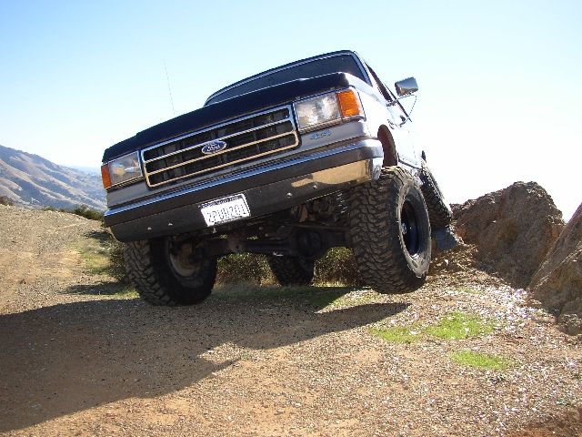 Lifted dark Ford SUV climbing a rock on a dirt trail, front tire raised on rock