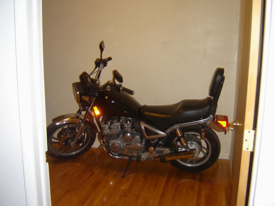 Black motorcycle with chrome accents and a passenger backrest, parked indoors on a wooden floor