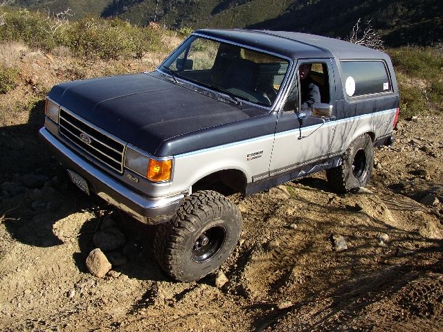 Blue and silver Ford Bronco SUV with lift and mud tires on rocky dirt trail