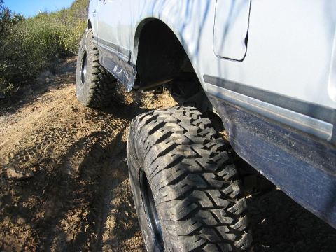 1989 Ford Bronco - This silver SUV, equipped with large off-road tires, navigates a dusty, uneven terrain.